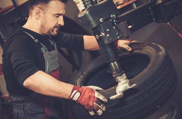 Dark-haired man puts tyre on rim with machine