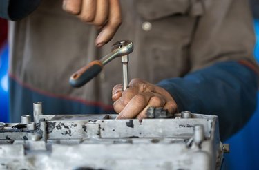 Male hands use a tool to fix something on a car engine