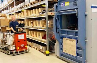 Truck driver navigating within a logistics area towards a baler machine, transporting cardboard waste for recycling